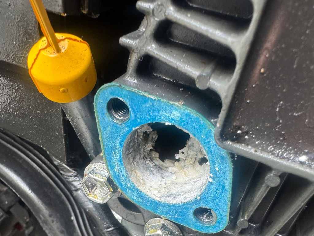 Åbnet flange på et motorhus med blå pakning, hvor boringen indeni er fyldt med hvide tærings- og saltaflejringer